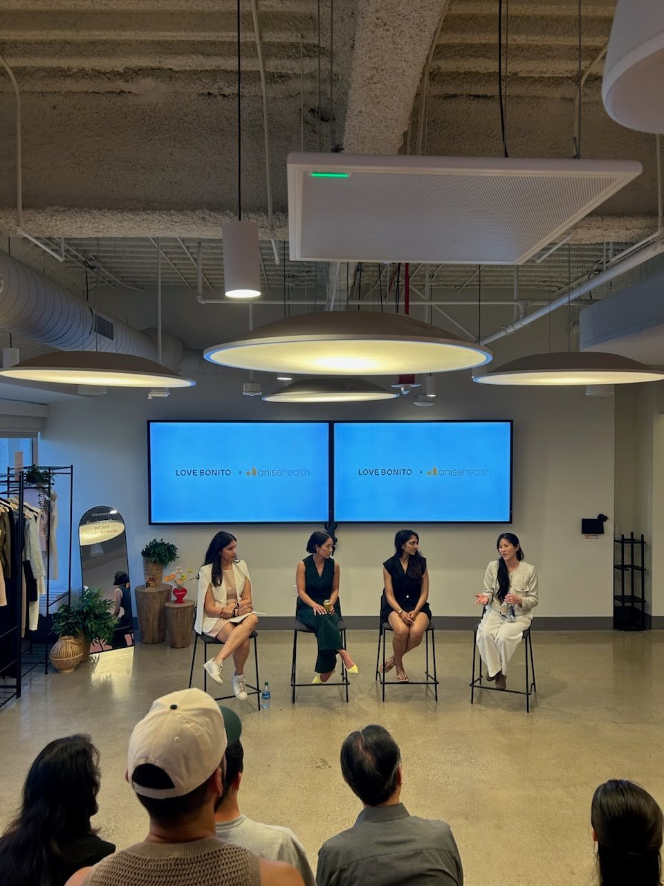 A panel of four feminine-presenting people sitting in chairs speaking to an audience with two large screens behind the panelists.